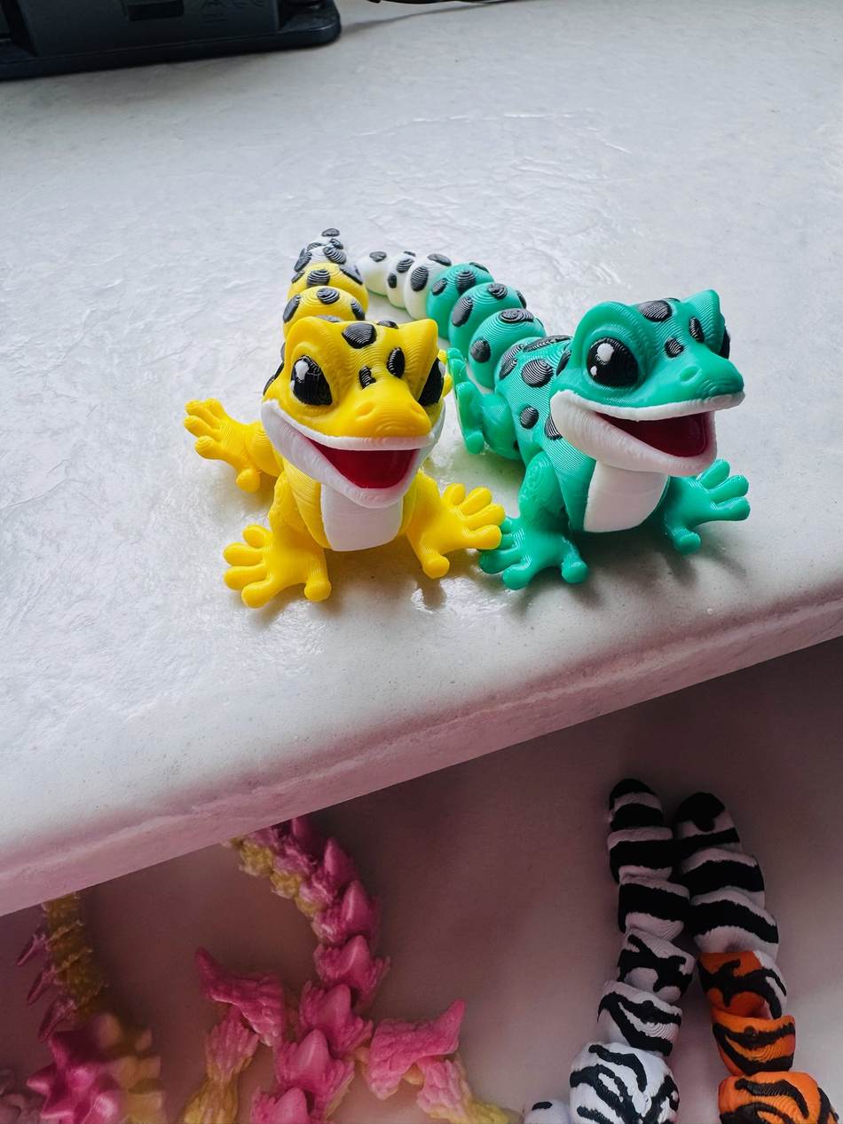 Zwei bunte artikulierte Gecko-Figuren in Gelb und Türkis